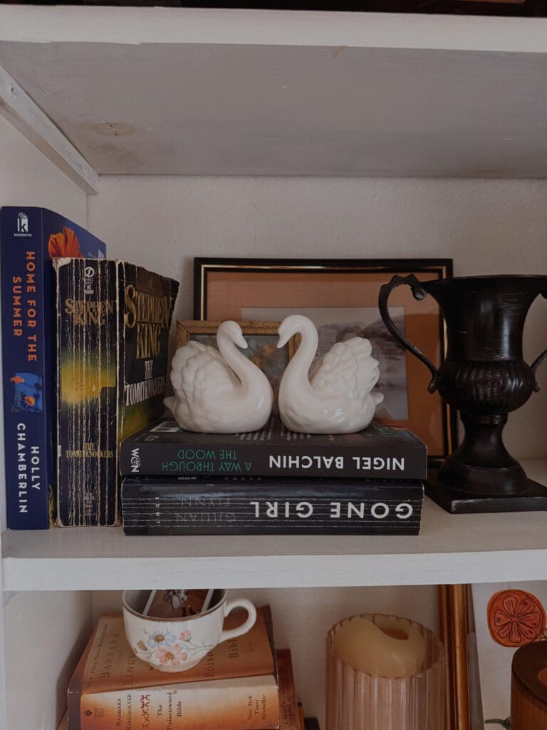 Swan decor on bookshelf with vintage books showing whimsical home design trend 2026