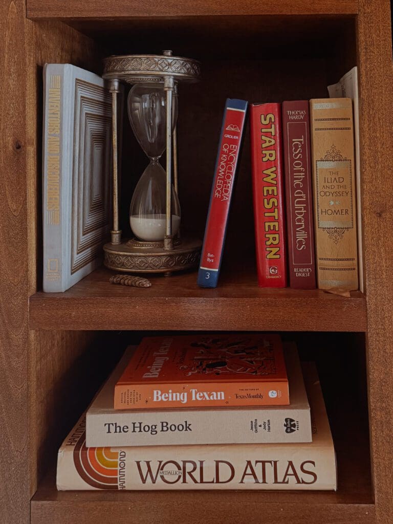 Vintage bookshelf styling with antique hourglass and classic literature Texas ranch house