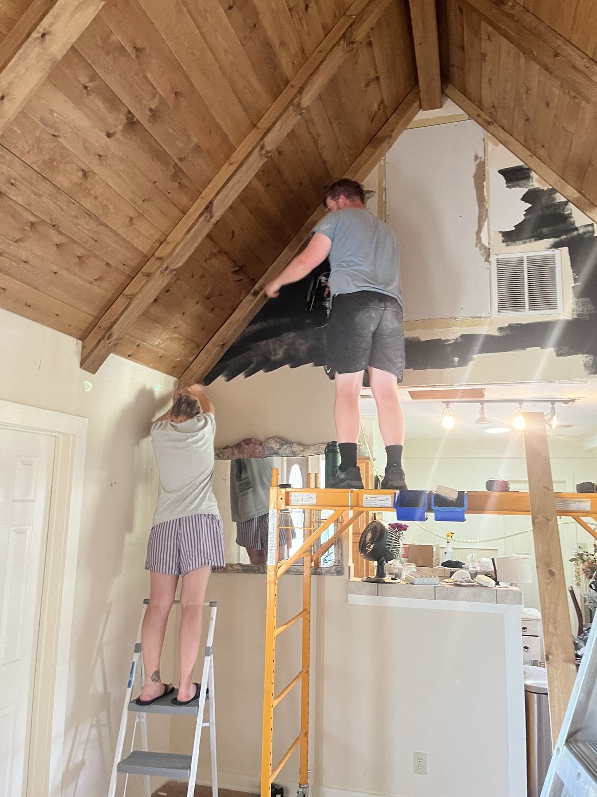 Family on ladders and scaffolding staining the wood ceiling and beams by hand.
