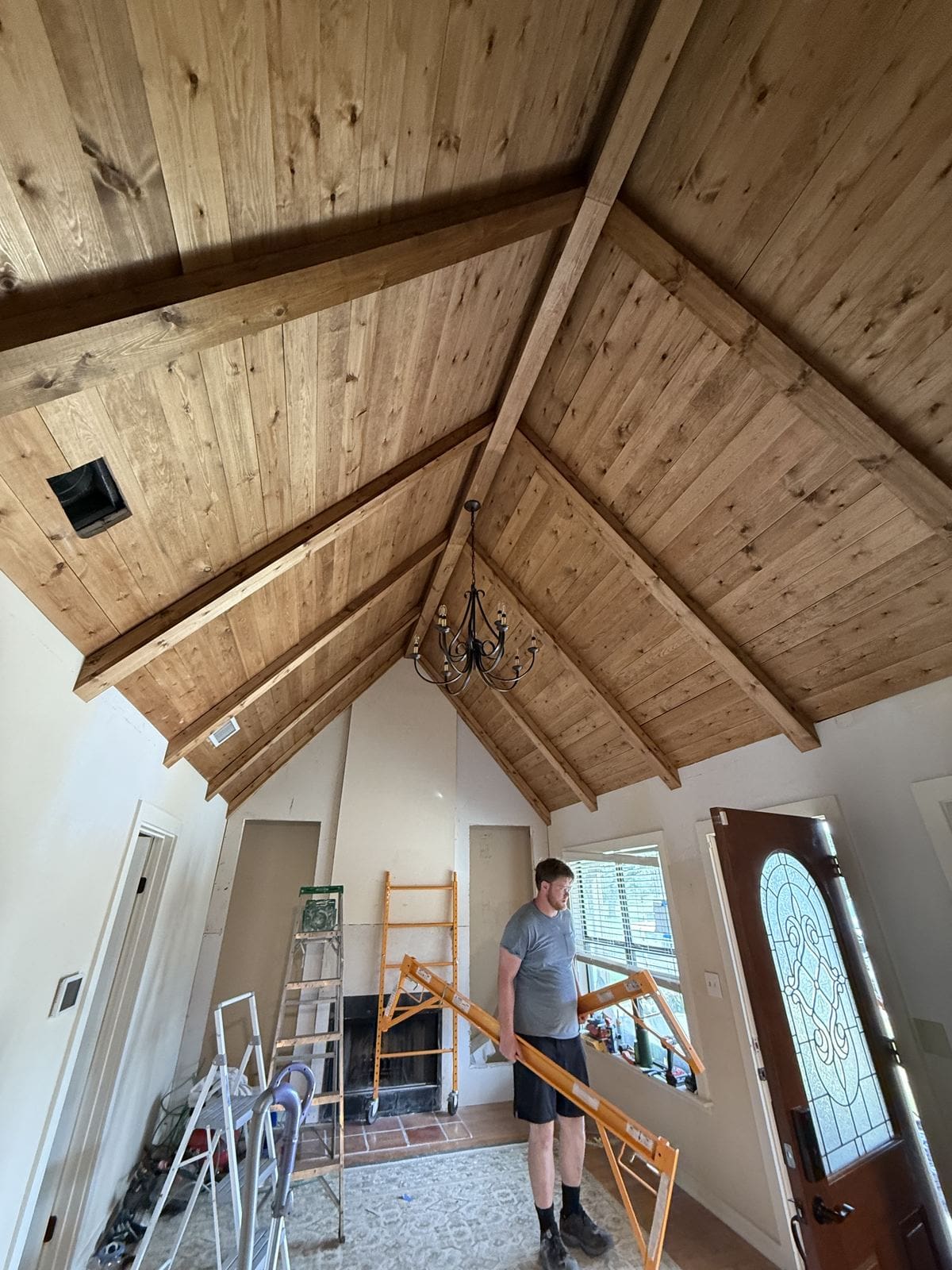 Wood ceiling stained in Early American with a new black chandelier hung at the peak.