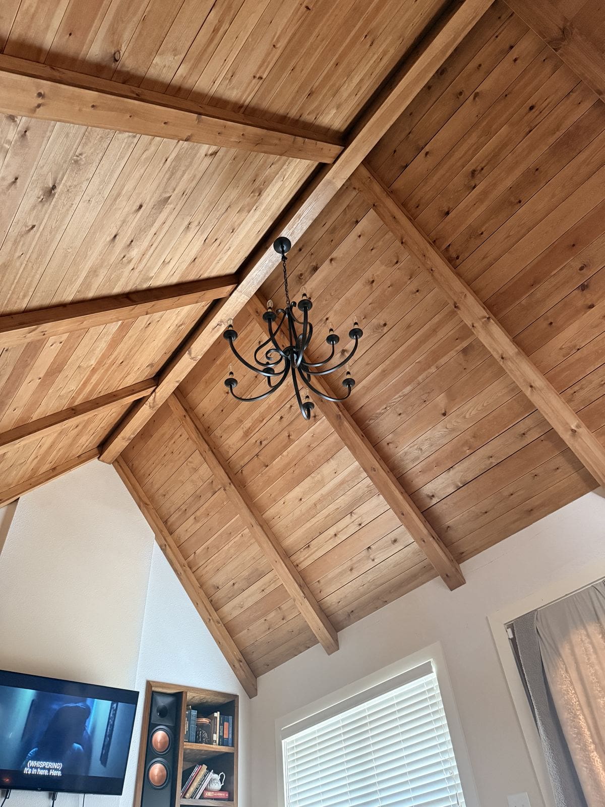 Finished stained pine vaulted ceiling with beams, a black chandelier, and styled built-in shelves.
