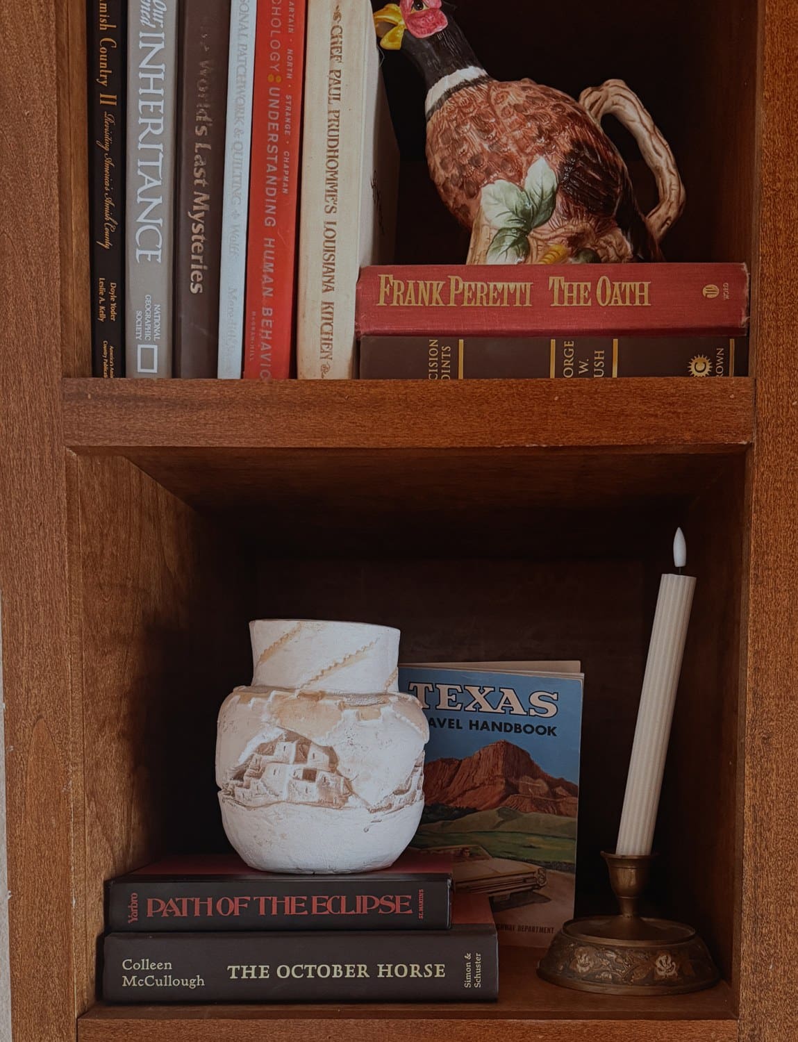 A thrifted styled bookshelf with vintage books, a ceramic vase, and a candlestick